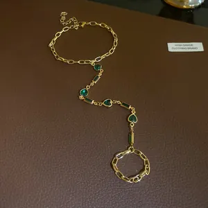 Detailed view of vintage gold hand chain bracelet with green heart and rectangular gems
