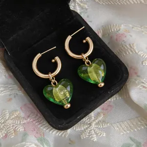 Gros plan de pendentifs cœurs en verre vert sur des créoles dorées dans une boîte noire.
