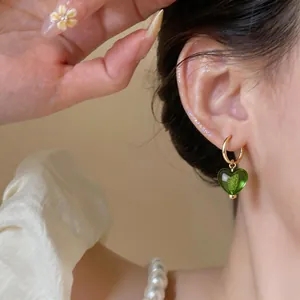 Gros plan d'une élégante boucle d'oreille cœur vert plaquée or sur une oreille de modèle
