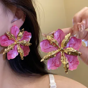 Gros plan de boucles d'oreilles fleurs en émail rose avec un centre en métal doré