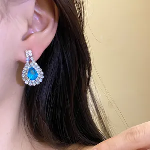 Detailed view of a teardrop-shaped blue gemstone earring worn by an Asian model in warm light.