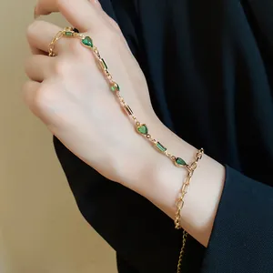 Close-up of a vintage gold heart ring bracelet with green gems on a hand.