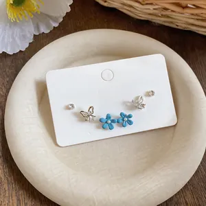 Detail shot of delicate rhinestone butterfly and blue flower oil-drop earring set on card.