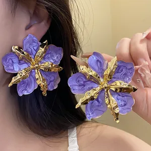 Gros plan sur des boucles d'oreilles fleurs en émail violet avec pétales dorés texturés.