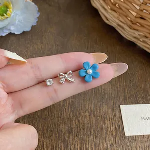 Close-up of drip oil blue flower, bow and rhinestone stud earrings set on finger