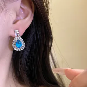 Detailed macro view of teardrop stud earring with blue stone and rhinestone border