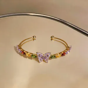 Close-up detail of a gold butterfly cuff bracelet with colorful teardrop zircon stones