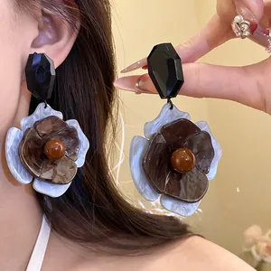 Close-up of retro brown acrylic flower dangle earrings shown on model ear and hand