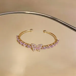 Detailed view of a gold-tone open bracelet featuring a butterfly motif and pink zircons.