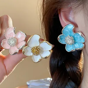 Détail de boucles d'oreilles clips fleurs en émail élégantes en rose, blanc et bleu.