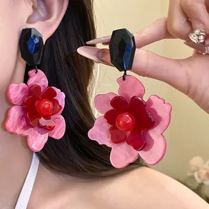 Close-up of layered pink acrylic flower drop earrings with black geometric stud.