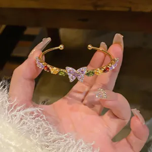 Close-up of elegant gold cuff bracelet with colorful zircon stones and purple butterfly