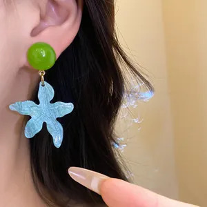 Detail shot of a light blue resin star flower earring with green stud on model