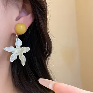 Close-up of vacation style resin flower earrings with a yellow sphere stud on a model's ear.