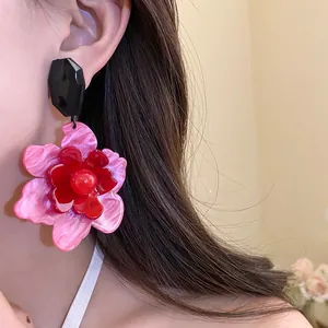 Close-up of vintage acrylic flower drop earrings in pink and red tones on model.