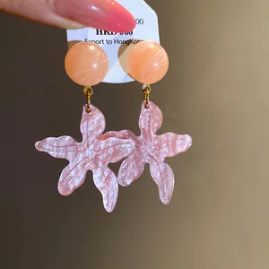 Close-up of pink resin starfish earrings with a shimmering finish and peach round studs