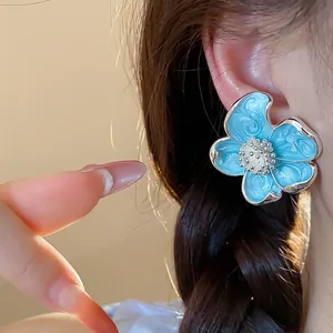 Détail en gros plan d'un clip d'oreille en émail bleu clair en forme de fleur.