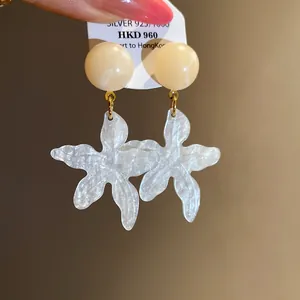 Macro detail of white shimmering resin star-shaped earrings with pearl studs