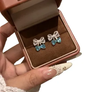 Elegant silver bow stud earrings with sparkling blue heart-shaped zircons in a box