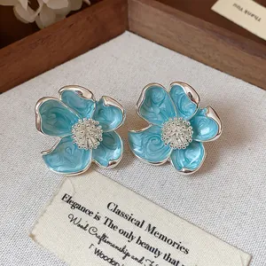 Gros plan de boucles d'oreilles clips fleurs en émail bleu sur fond décoratif vintage.