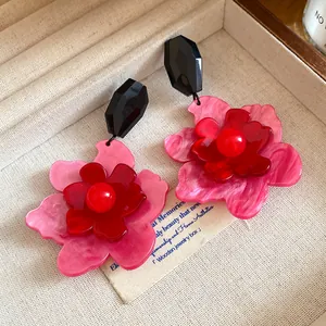 Close-up of retro acrylic flower dangle earrings with layered pink and red petals.