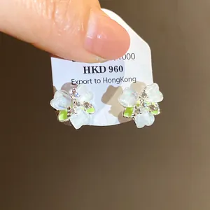 Detail view of dainty white forest-style flower stud earrings with green accents
