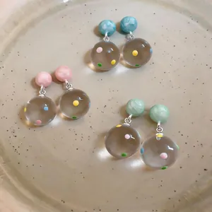 Close-up of transparent resin earrings with colorful polka dots in pink, blue, and green.