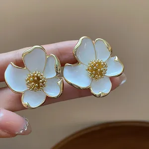 Détail de boucles d'oreilles fleurs en émail blanc avec pistils dorés au style minimaliste