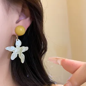 Close-up of beach-style resin earrings with yellow bead and white starfish design on model's ear