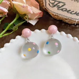 Macro view of clear resin drop earrings with colorful polka dots and pink studs.