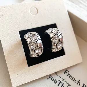 Dettaglio ravvicinato di eleganti orecchini a C in argento con motivo esagonale e strass