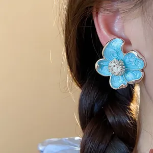Gros plan détaillé de boucles d'oreilles à clip fleur en émail bleu sur un mannequin