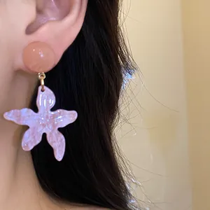 Close-up of pink resin starfish earrings worn by a model in a summer vacation style.