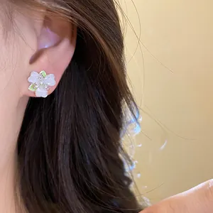 Detailed close-up showing a delicate white flower stud earring with green accents on an ear.
