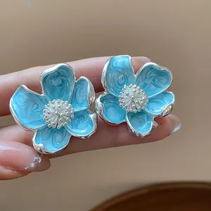 Vue détaillée des clips d'oreilles fleurs en émail bleu frais avec accents argentés d'été.