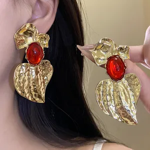 Close-up of oversized gold textured heart earrings with large red resin stones