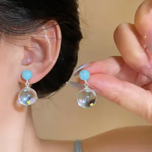 Close-up of clear resin earrings with colorful polka dots and light blue studs