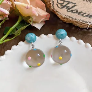 Close-up of clear resin sphere earrings with colorful polka dots on a white plate