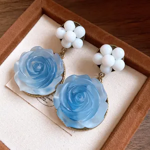 Macro detail of French retro blue resin rose earrings with white bead flower studs