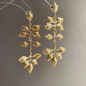 Vue macro détaillée de boucles d'oreilles à pompons en feuilles dorées texturées vintage.