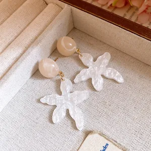 Detail of white marbled resin flower earrings with beige stud in a jewelry tray