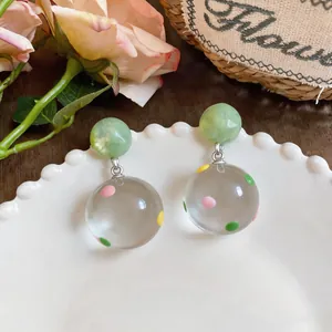 Detail view of clear resin drop earrings with colorful polka dots on a white plate.