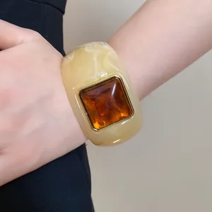 Detail view of a luxury minimalist cream marbled acrylic bangle with amber square resin insert