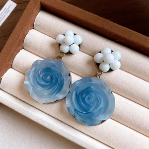 Close-up detail of 3D blue resin rose earrings with white bead accents.