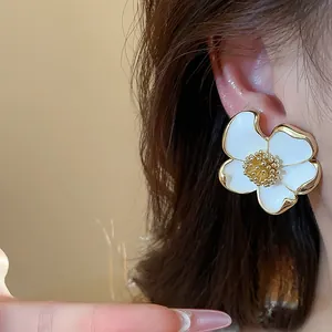 Vue détaillée d'une boucle d'oreille fleur en émail blanc avec bordure dorée sur l'oreille