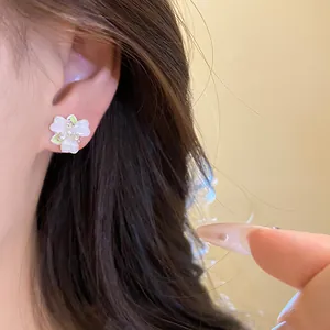 Close-up detail of delicate white flower stud earrings with green accents worn on ear