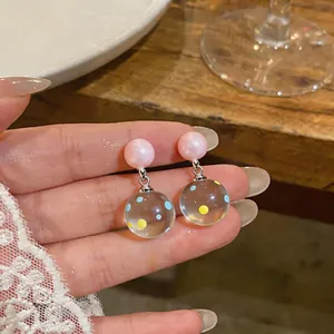 Close-up of clear resin earrings with blue and yellow polka dots and pink pearl studs.