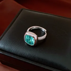 Détail d'une bague avec pierre verte taille coussin sur un écrin de bijoux noir chic