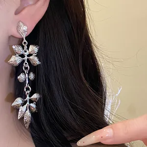 Gros plan de boucles d'oreilles pendantes en feuilles plissées argentées portées à l'oreille