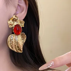 Close-up of an exaggerated gold hammered earring with a red resin stone on ear